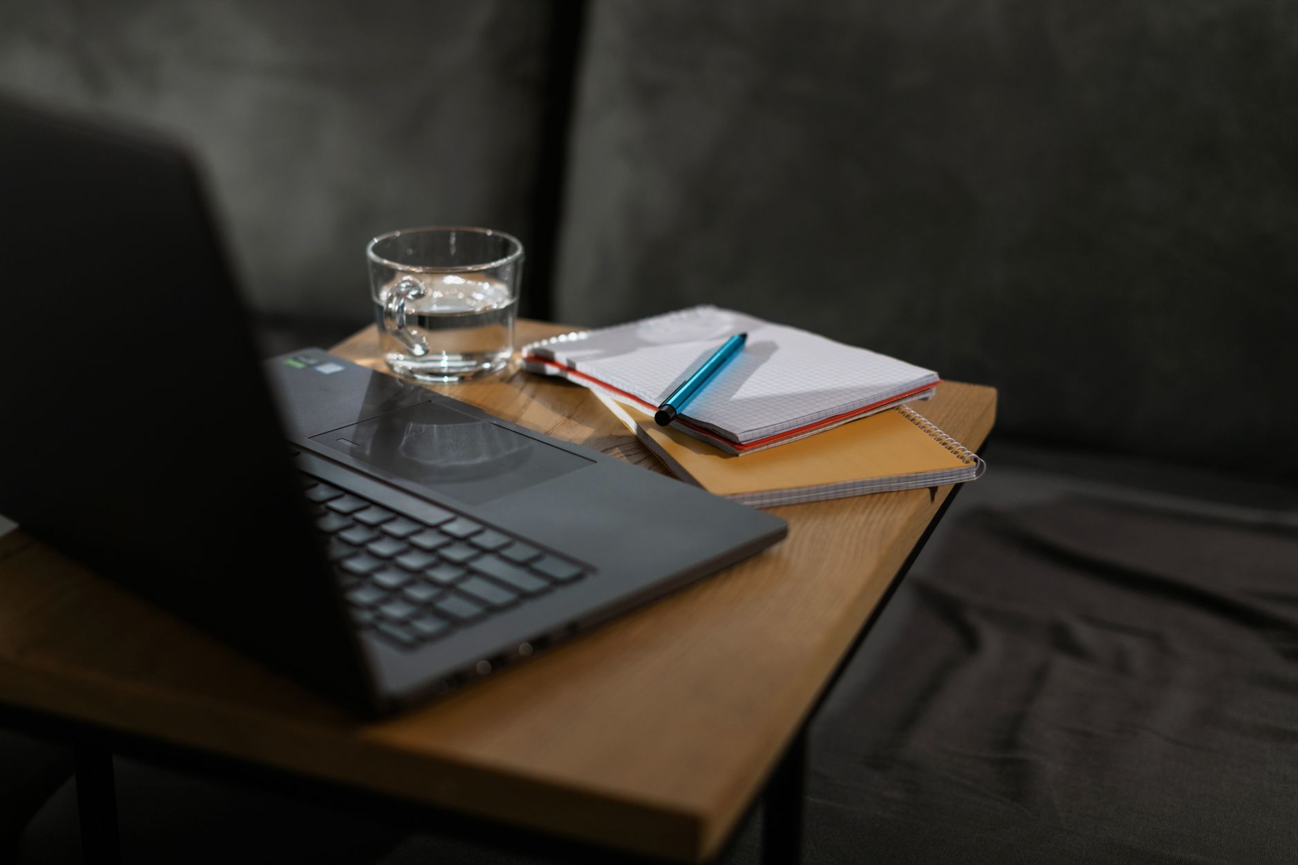 Et minimalistisk hjemmekontor med en laptop, notatbøker og et glass vann på et trebord.